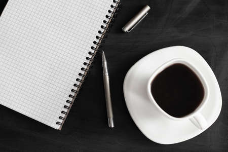 White cup of strong black coffee with metal pen and notepad on black surface close upの写真素材