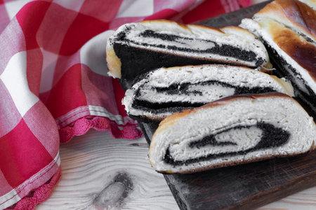 Baked roll with poppy seeds, three chopped pieces close-up on a wooden background with a red and white clothの写真素材