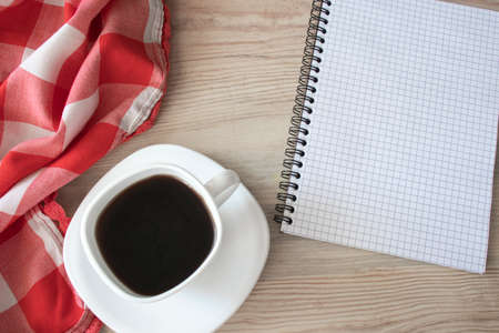 White cup of strong black coffee with red-white cloth and notepad on wooden surface close upの写真素材