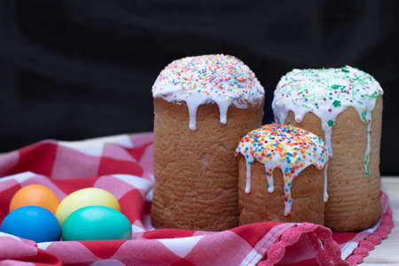 Three baked Easter cakes decorated with sprinkling sugar, four colored chicken eggs on a red and...