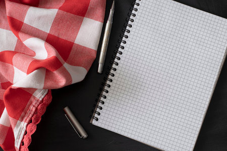 Notepad, metal pen and red-white cloth on a black surface close-upの写真素材