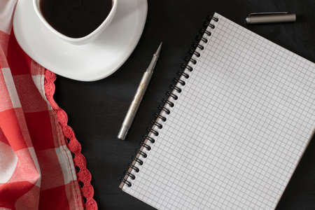 White cup of strong black coffee with metal pen, notepad and red-white cloth on black surface close upの写真素材