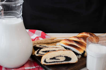 Baked roll with poppy seeds, glass decanter and glass cup with milk, close upの写真素材