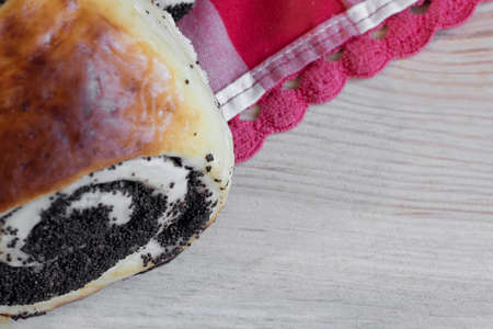 Roll with poppy seeds close-up on a wooden background with red and white clothの写真素材