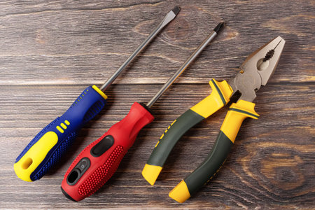 two screwdrivers and pliers on a wooden background