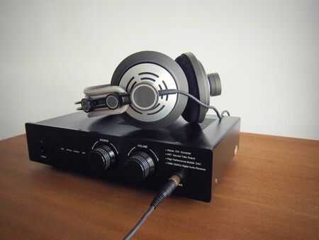Black DAC Headphone amplifier with connected headphones on the wooden desk