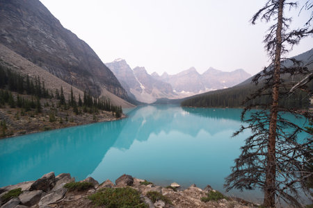 Lake Moraine Turquoise Water Mirror Surface with Canadian Rocky Mountains Behind, Summer Day Haze, Banff National Park, Alberta, Canadaの写真素材