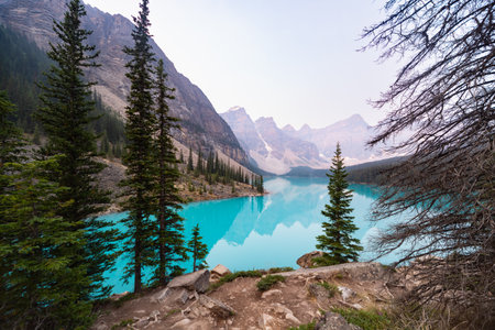 Lake Moraine Turquoise Water Mirror Surface with Canadian Rocky Mountains Behind, Summer Day Haze, Banff National Park, Alberta, Canadaの写真素材