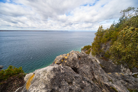 Rugged Rocky Limestone Cliff Surrounded by Turquoise Water of Lake Huron. Stormy Autumn Day near Indian Head trail, Ontario, Canadaの写真素材