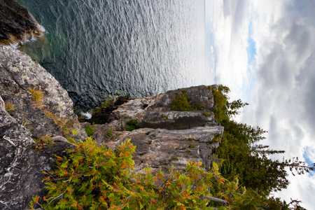 Limestone Wall Rugged Rocky Cliff with Trees Surrounded by Turquoise Water of Lake Huron, vertical shot during dramatic stormy autumn day at Indian Head Trail, Ontario, Canadaの写真素材
