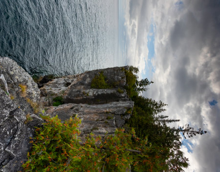 Limestone Wall Rugged Rocky Cliff with Trees Surrounded by Turquoise Water of Lake Huron, vertical shot during dramatic stormy autumn day at Indian Head Trail, Ontario, Canadaの写真素材