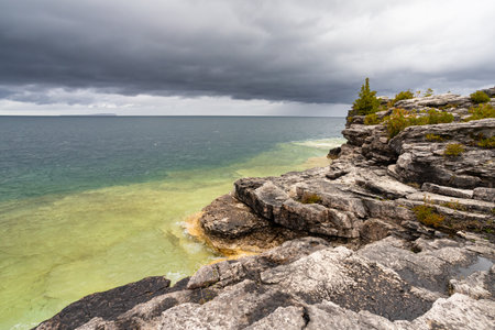 Rugged Rocky Limestone Cliff Surrounded by Turquoise Water of Lake Huron. Stormy Autumn Day near Cyprus Lake, Ontario, Canadaの写真素材