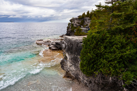 Rugged Rocky Limestone Cliff Surrounded by Turquoise Water of Lake Huron. Stormy Autumn Day near Indian Head trail, Ontario, Canadaの写真素材