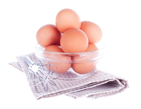Fresh eggs in the glass bowl, steel whisk and napkin on the white backgroundの写真素材