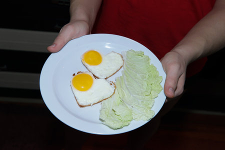 scrambled eggs in the shape of hearts on a plate, with lettuce leaves in the hands of a young man. ideas on how to surprise and please your beloved. breakfast is like a declaration of love. top view.の写真素材