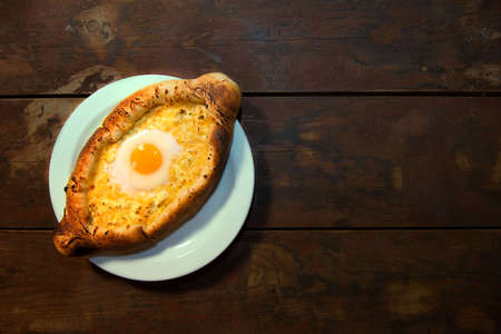 Close-up of khachapuri with egg on a dark background, Georgian cuisine dish, vegan food. Adjarian khachapuri. Adjarian khachapuri on a close-up on a wooden table.の写真素材