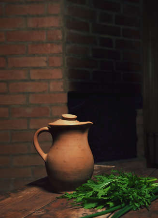 Old rustic wine jug on a wooden table.Ceramic clay terracotta jug.the composition is filled with greenery. conceptual photo with reflection of national color.dark background, lots of advertising spaceの写真素材