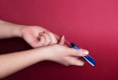 Man using a glucometer checking blood sugar levels. Diabetes concept on red background. emphasis on the problem of early detection and prevention of disease. empty space for informationの写真素材