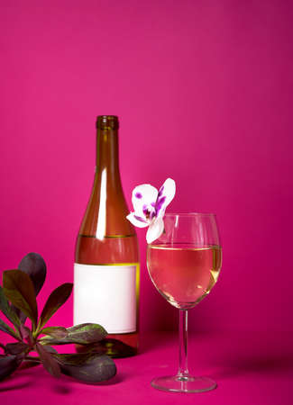 a glass of wine on a bright background with a bottle of wine and delicate orchids. ready for layout and Mockup. label for any name and variety. advertising of wines and restaurantsの写真素材