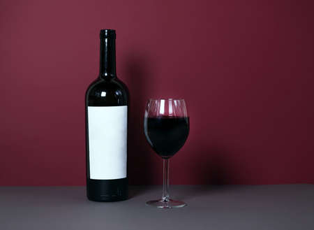 a glass of red wine on a burgundy background with a bottle of wine in the background. stylish wine advertising. suitable for advertising a wine restaurant. mokap. banner.の写真素材
