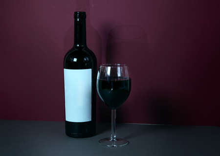 a glass of red wine on a burgundy background with a bottle of wine in the background. stylish wine advertising. suitable for advertising a wine restaurant. mokap. banner.の写真素材