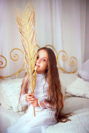 a girl sits on her bed with a decorative golden firebird feather. the concept of a lifestyle. vintage. advertising comfort and attitude to life.の写真素材