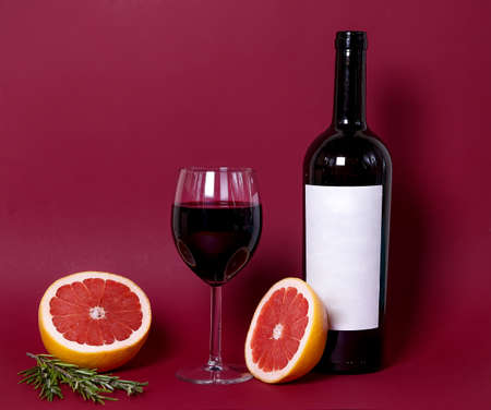 a glass of red wine on the background with a bottle under the layout.red grapefruit and rosemary sprigs add a special charm to the composition.copy space. advertising a restaurant, winery, or wine listの写真素材
