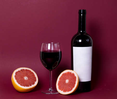 a glass of red wine on a burgundy background. red grapefruit and rosemary sprigs give the composition a special unique style. copy space. advertising a restaurant, winery, or wine list.の写真素材
