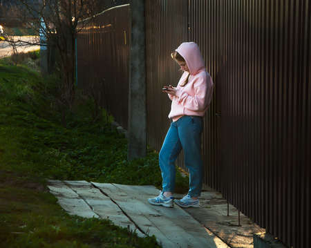 A young girl, waiting With a Mobile Phone For a Trip, stands near her house. the concept of taxi advertising and on-line service advertisingの写真素材