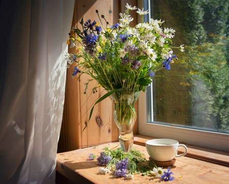 A soft, concentrated bouquet of flowers in an old vase on the windowsill in the morning sun. Next to him on the windowsill is a mug of natural milk, a selective soft focus. Rustic style, simplicity.の写真素材