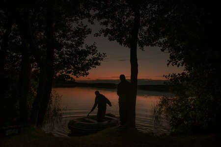 night fishing. the boat docks at the shore of the night lake, the father and son are returning from fishing. silhouettes. night shooting, soft selective focusingの写真素材