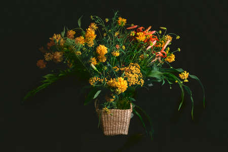 A fancy bouquet of yellow wildflowers with lilies on a dark background. Still-life. In the style of ancient Dutch masters. Large format for printing paintings in the interiorの写真素材