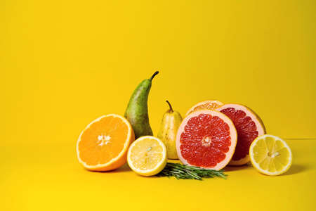 Tropical fruits grapefruit, orange and lime on a yellow background with rosemary sprigs. ideal for advertising healthy food, a blog about vitamins and a healthy lifestyle. copy spaceの写真素材