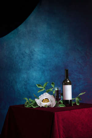 Retro composition with a glass of red wine against a textured blue wall and red velvet with a white peony. The concept of a vintage party or Thanksgiving. conceptually, in the style of minimalism.の写真素材