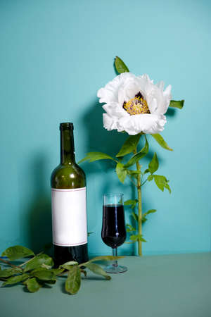 Retro composition with a glass of red wine. white peony on a soft turquoise background, vintage shade. Restrained. side view. Flower postcard, poster. conceptually, in the style of minimalism.の写真素材