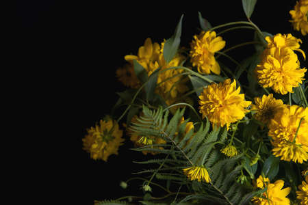 A bouquet of beautiful yellow flowers with fern leaves in close-up on a dark background. Abstract...