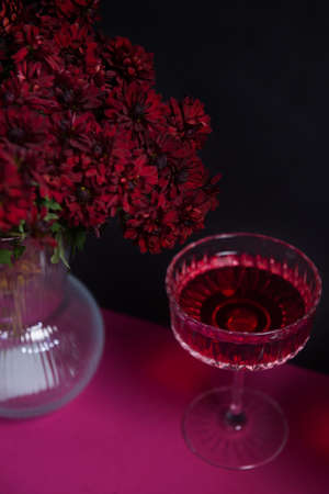 Still life of grapes, filled glass of wine, red flowers on a bright red background. Stylish and conceptual, the concept of a romantic holiday. sexuality and femininity combined with fragrant wine.の写真素材