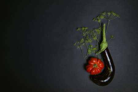 Creative layout of vegetables, dill with eggplant and ribbed tomatoes on a dark background.Flat lay....