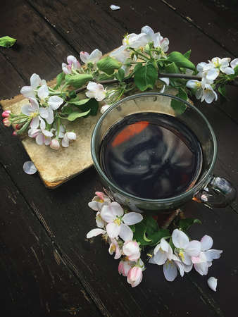 A cup of tea with spring cherry blossoms and an old book on a wooden background. the photo is perfect for social networks, illustrations in a personal blog. poster. advertisement. chinese teaの写真素材