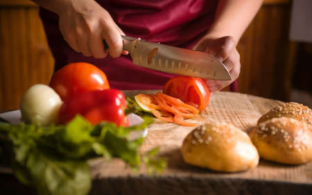 Close-up of a woman cutting vegetables with a sharp kitchen knife. Cooking healthy organic food in the home kitchen. The concept of a natural clean diet and a healthy lifestyle. selective focusの写真素材