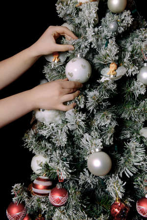 Decorating the Christmas tree. Hand holding a Christmas tree decoration. Christmas and New Year celebration concept. Cropped hands of girl decorate and hang from tree. Copy spaceの写真素材