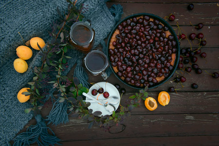 Cherry pie with fresh cherries on a rustic wooden background. still life with a pie, cups of tea and fruit on a wooden table. cozy atmosphere and romantic breakfast for two in natureの写真素材