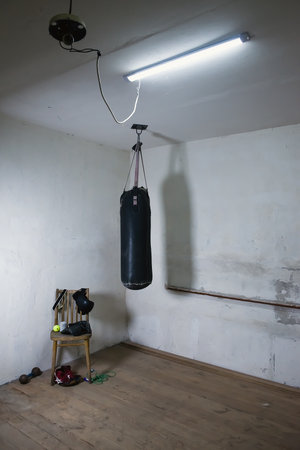 a punching bag in an empty boxing gym with a bare orange wall in the background. An old black boxing bag hanging on a rusty gray wall. the hall where the champions begin to train. copy spaceの写真素材