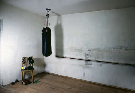 a punching bag in an empty boxing gym with a bare orange wall in the background. An old black boxing bag hanging on a gray shabby wall. the hall where the champions begin to train. copy spaceの写真素材