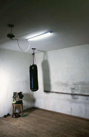 a punching bag in an empty boxing gym with a bare orange wall in the background. An old black boxing bag hanging on a gray shabby wall. the hall where the champions begin to train. copy spaceの写真素材