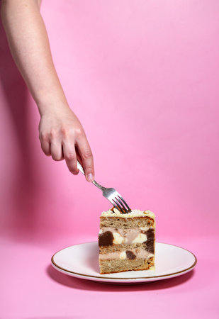The girl's hand wants to taste a piece of cake on a plate in white chocolate, decorated with nuts,...