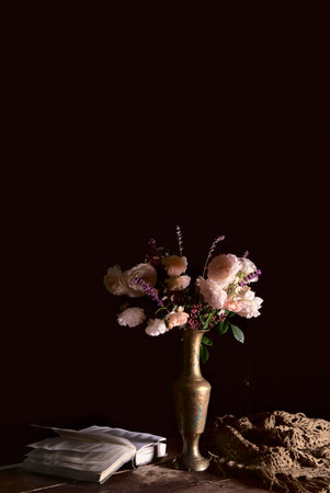 a bouquet of white roses, with the addition of lavender, sprigs of barberry to the floral arrangement. still life in the classical style. a bouquet of flowers in a vintage vase on a dark background with an open book on the table.の写真素材
