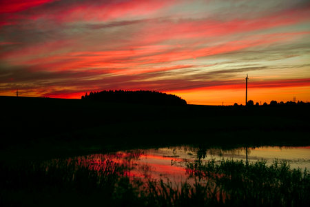 The sky after sunset is the background. A panorama of a colorful magnificent sunset in the countryside over hills, fields and a lake. sunset reflection in the lake. copyspace. atmospheric photoの写真素材