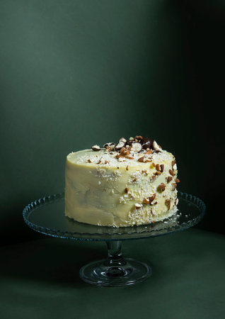 Festive banana cake in white chocolate,decorated with nuts, cookies and chocolate on a dark green...