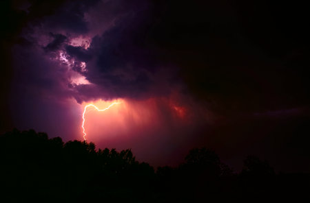 Fiery lightning pierces the sky, densely covered with black clouds. The strongest electric charge hits the ground. The concept of the apocalypse, catastrophe, war.battles of good and evil.thunderstormの写真素材